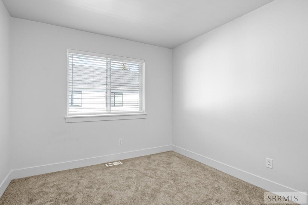 Empty bedroom with beige carpet and a window fitted with horizontal blinds.