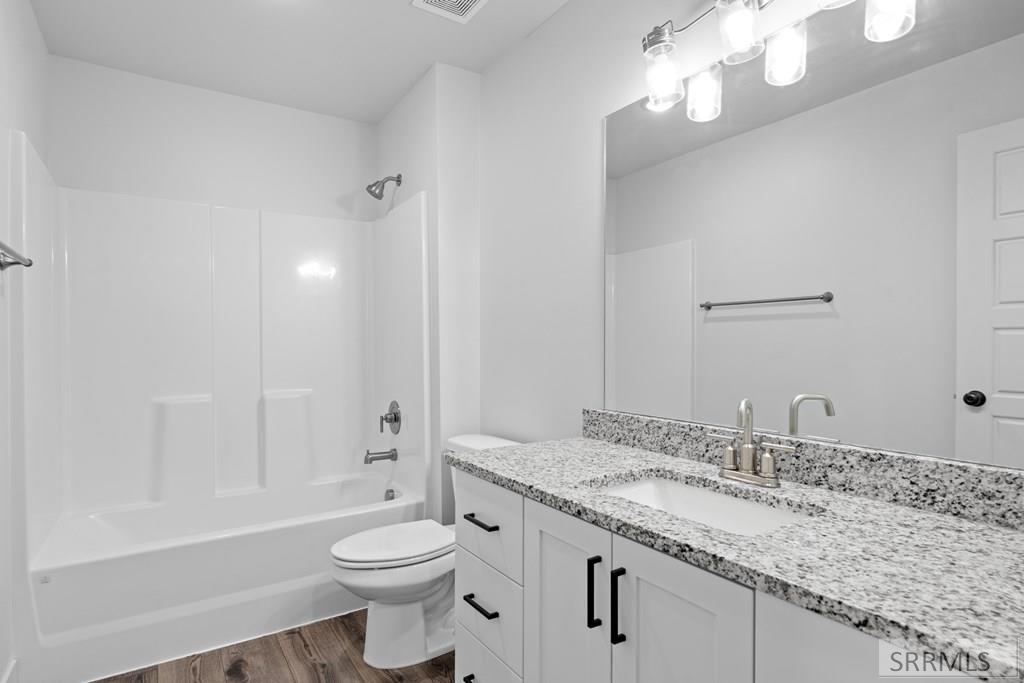 Bathroom with a white tub and shower beside a granite-topped vanity and large mirror.
