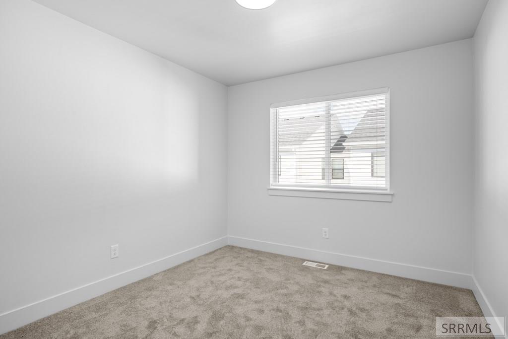 Empty carpeted room with gray walls and a window overlooking a neighboring house.