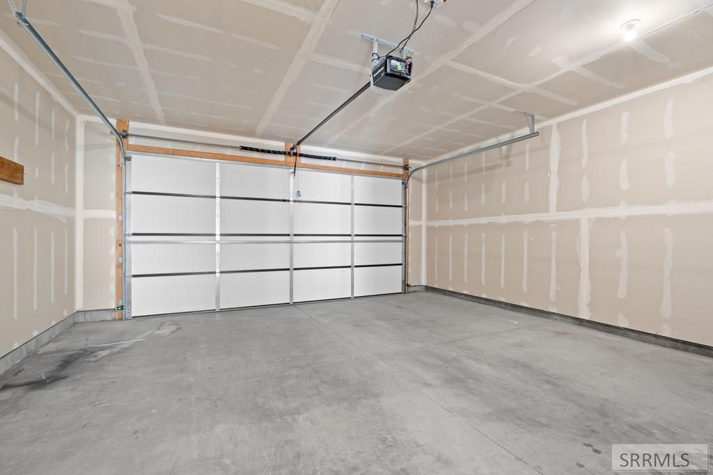 Empty garage with a wide white overhead door, concrete floor, and unfinished drywall.