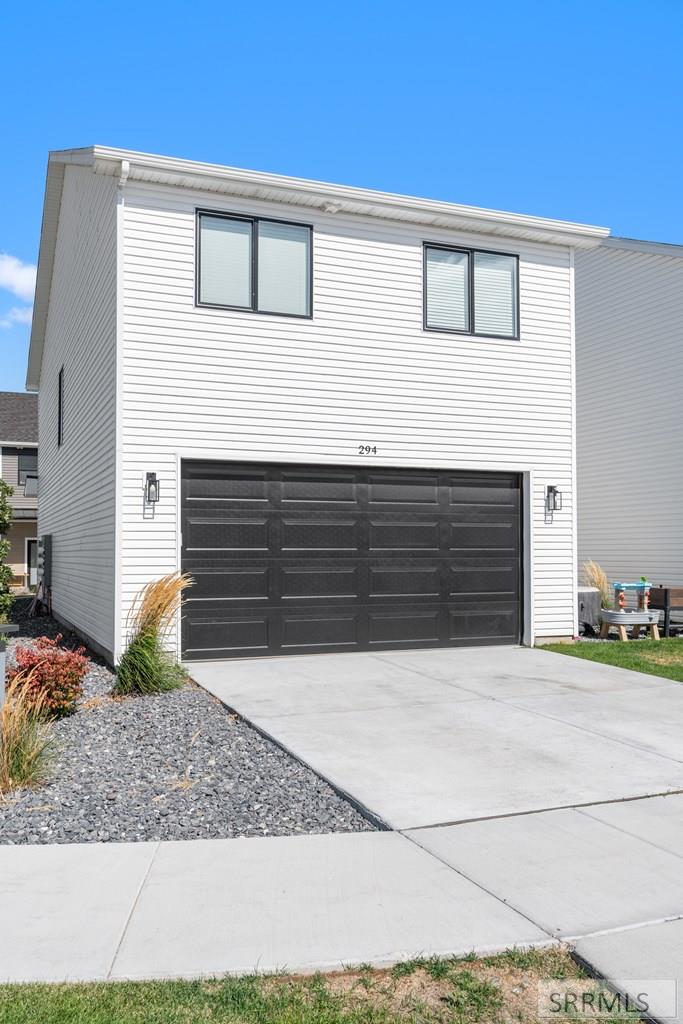 Two-story white-sided home with a black double garage door and broad concrete driveway.