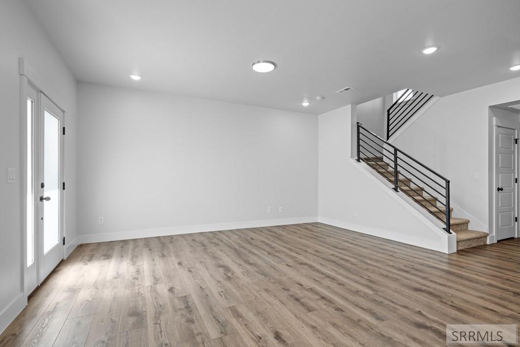 Vacant living room with gray wood-look floors and a carpeted staircase with black railing.