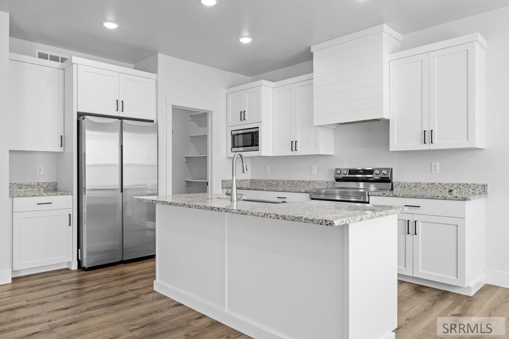 Kitchen with a large stone-topped island, white cabinets, and stainless steel appliances.