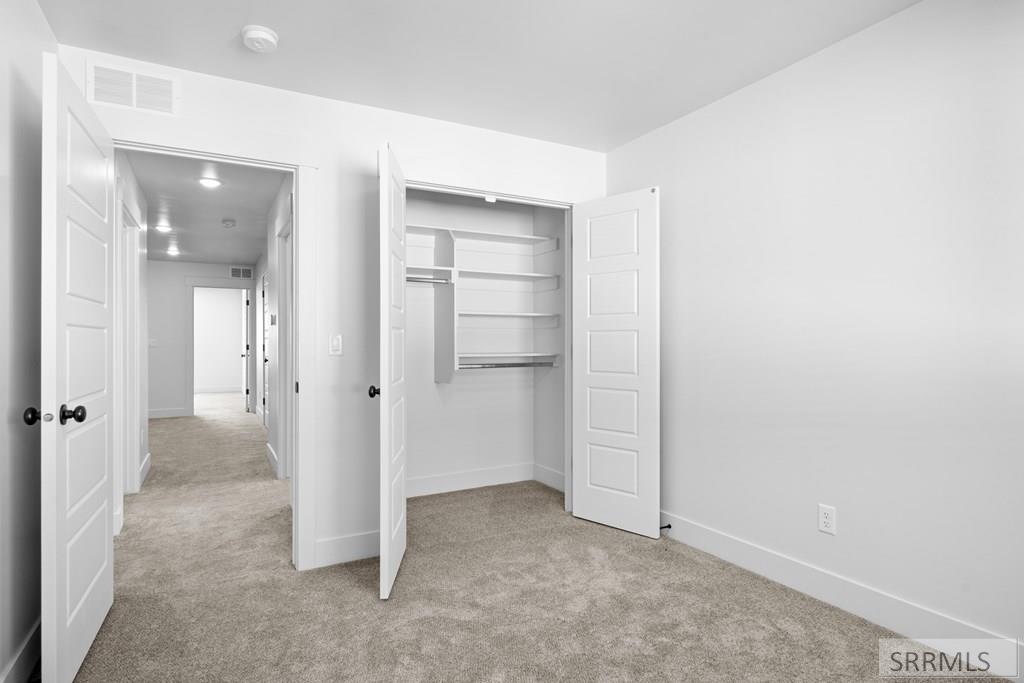 Empty carpeted bedroom with an open shelved closet and hallway beyond.