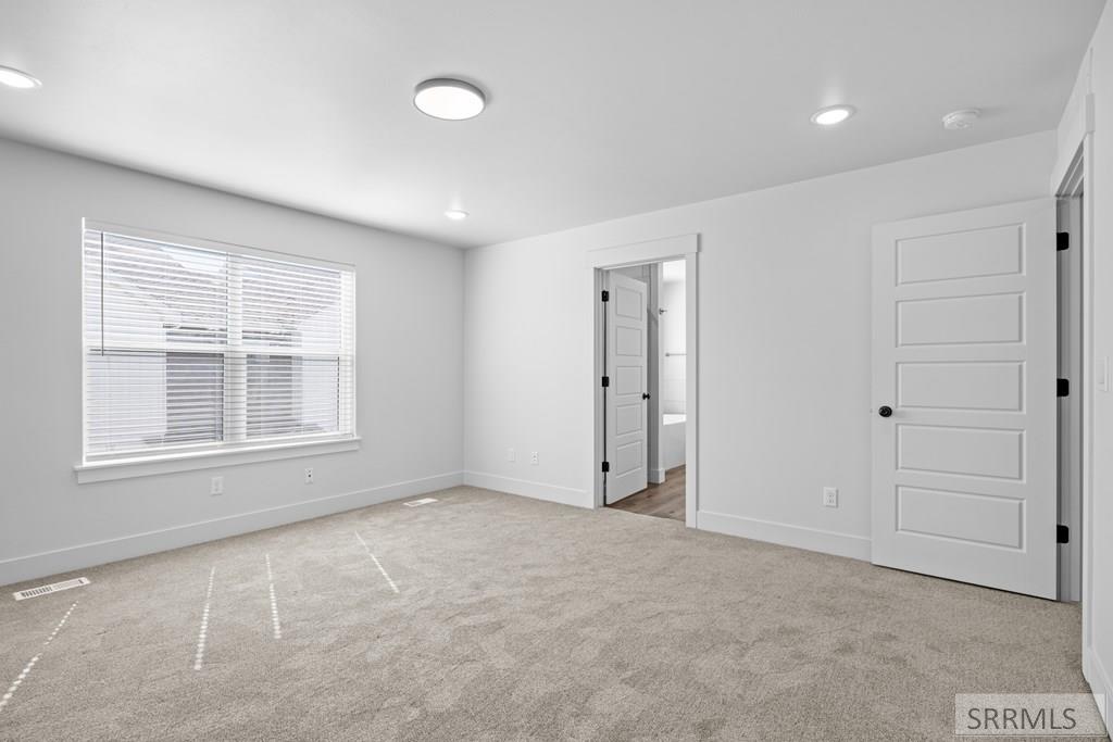 Empty bedroom with carpet, a wide blinded window, recessed lights, and two open doors.