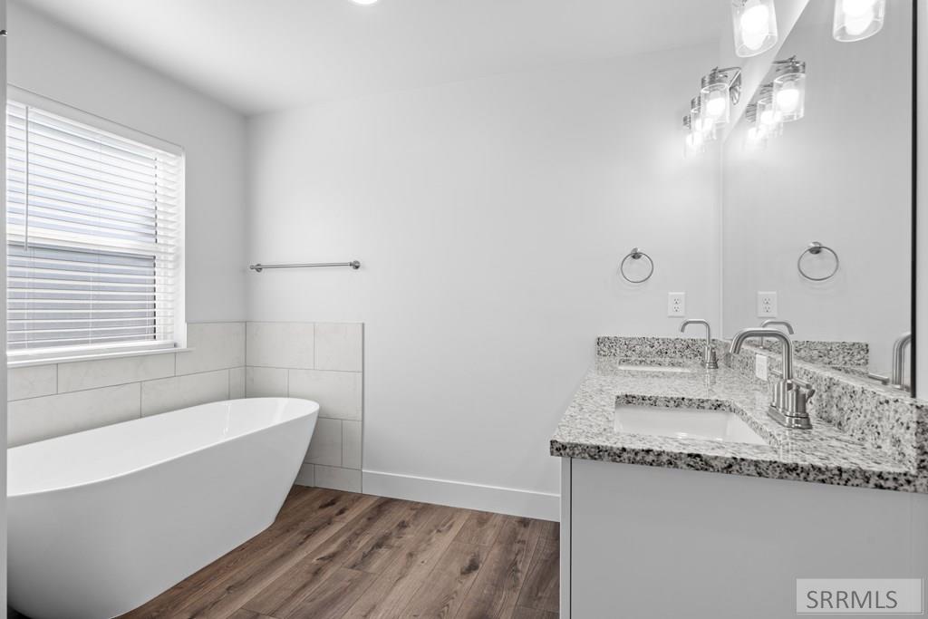Bathroom with a freestanding tub, double vanity, large mirror, and wood-look flooring.