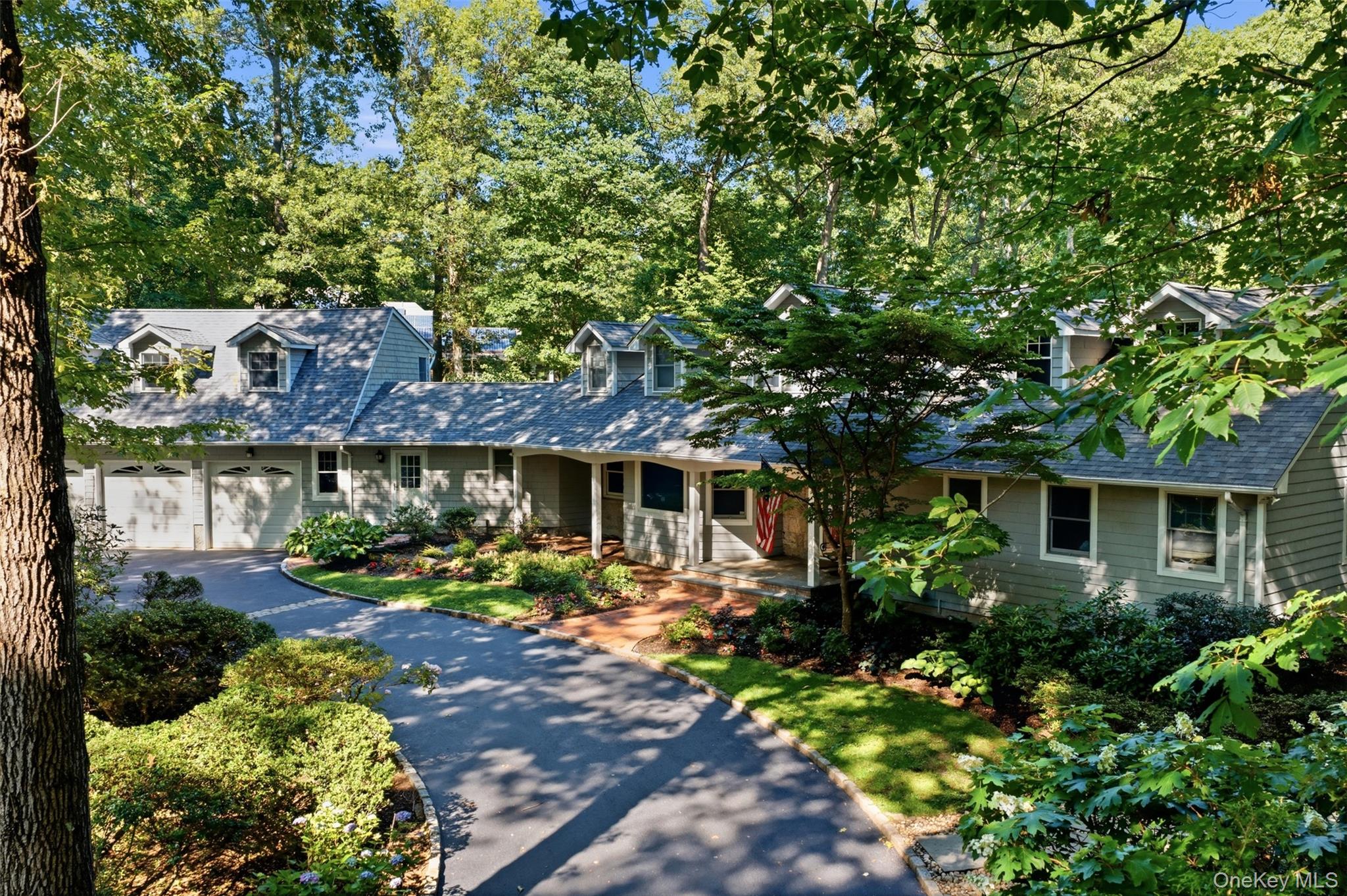 Gray house with a curved driveway, two-car garage, and leafy landscaped grounds.