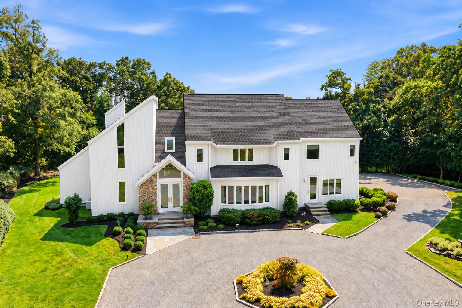 White modern home with a stone entry, landscaped grounds, and a circular driveway.