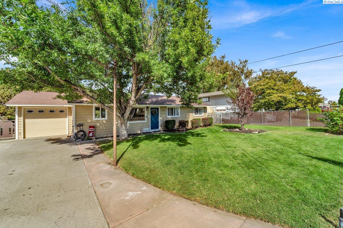 Single-story home with an attached garage, blue front door, and mature tree shading the lawn.