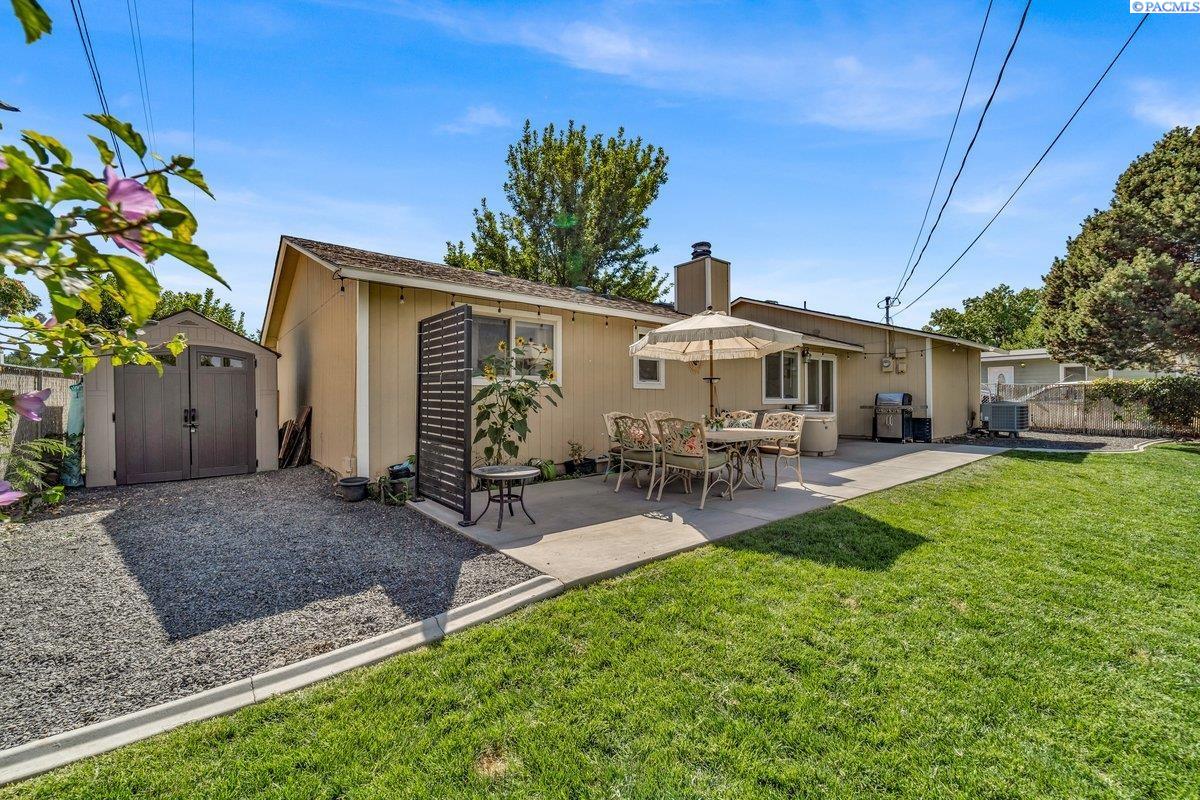 Backyard with a patio dining set and umbrella beside a single-story home and storage shed.