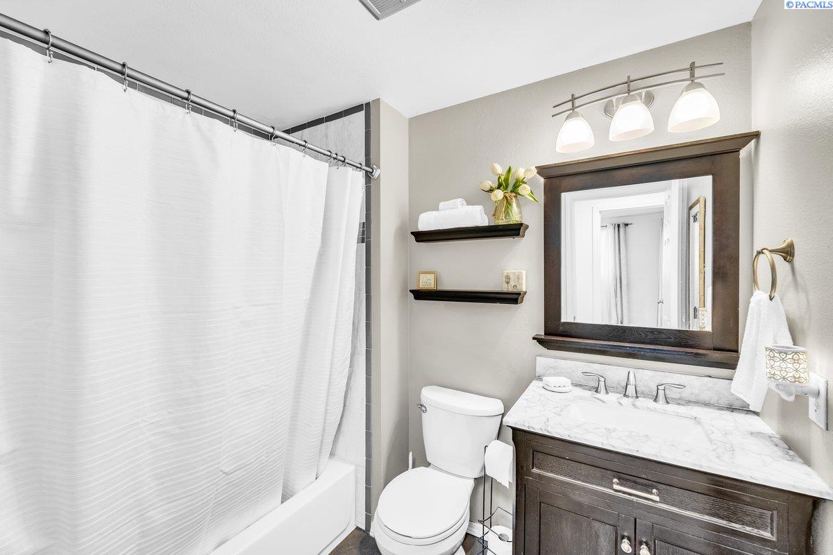 Bathroom with a curtained tub, toilet, and dark wood vanity beneath a large framed mirror.