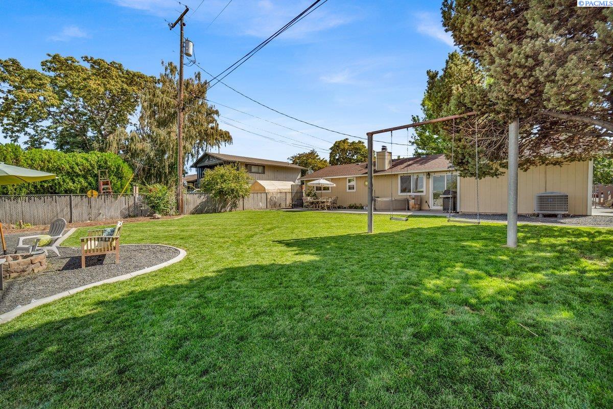 Backyard with a broad lawn, fenced seating area, and metal swing frame beside a single-story home.