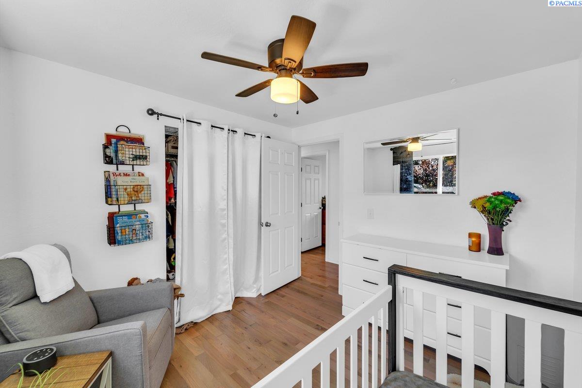 Bedroom with a white dresser, gray armchair, wood floors, and a crib railing in the foreground.