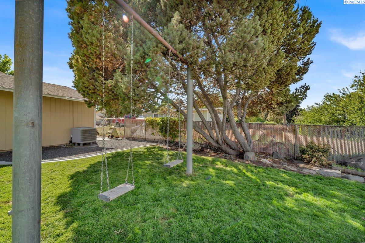 Backyard lawn with two hanging swings beneath mature pine trees and a metal fence.