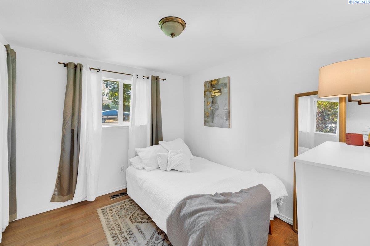 Furnished bedroom with a white bed, gray throw, and curtained window.