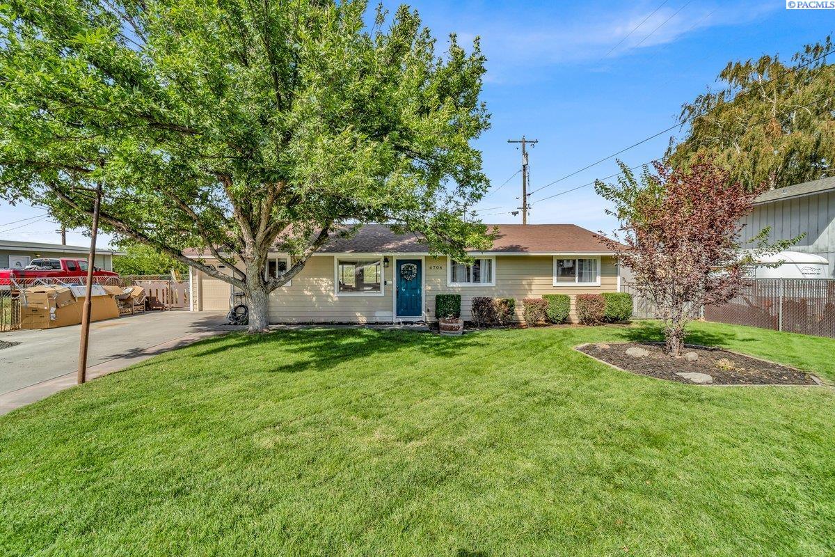 Single-story home with a blue front door, broad lawn, and mature shade tree.