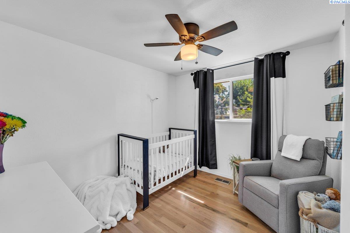 Nursery with a white crib, gray armchair, hardwood floors, and black curtains around the window.