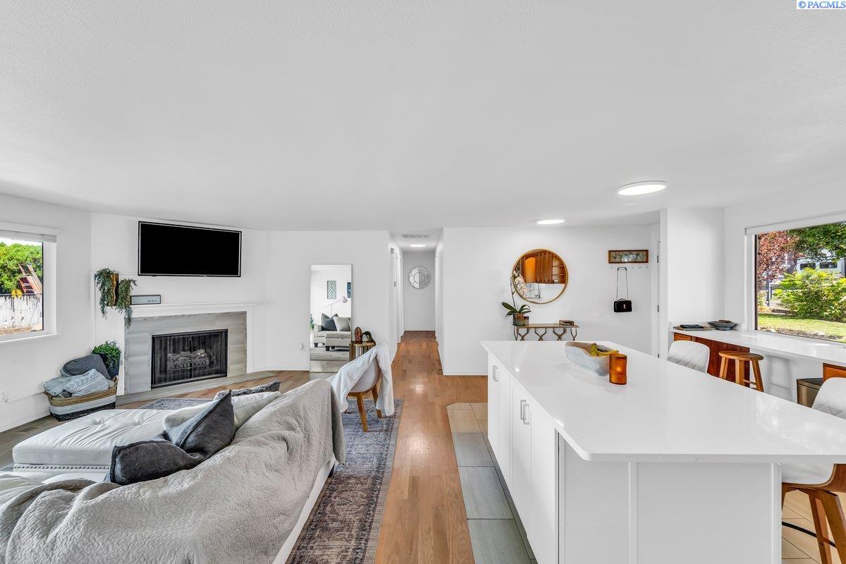 Open-plan living room and kitchen with a white island, fireplace, and large windows.