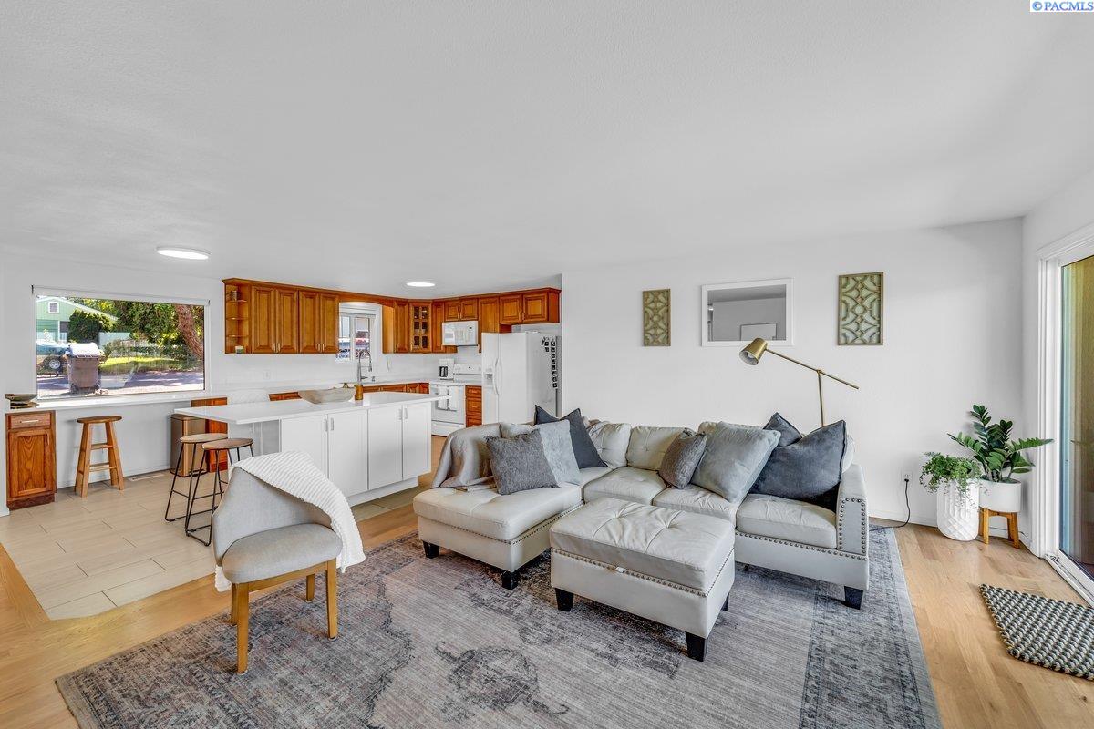 Open-plan living room and kitchen with a gray sectional, patterned rug, and warm wood cabinets.