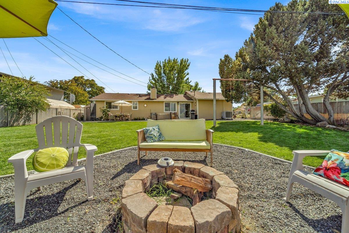 Backyard with a stone fire pit and seating area overlooking a lawn and single-story home.