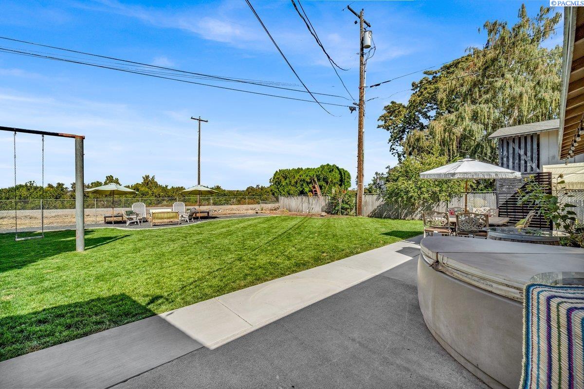 Backyard with a broad green lawn, swing set, patio seating, and hot tub.
