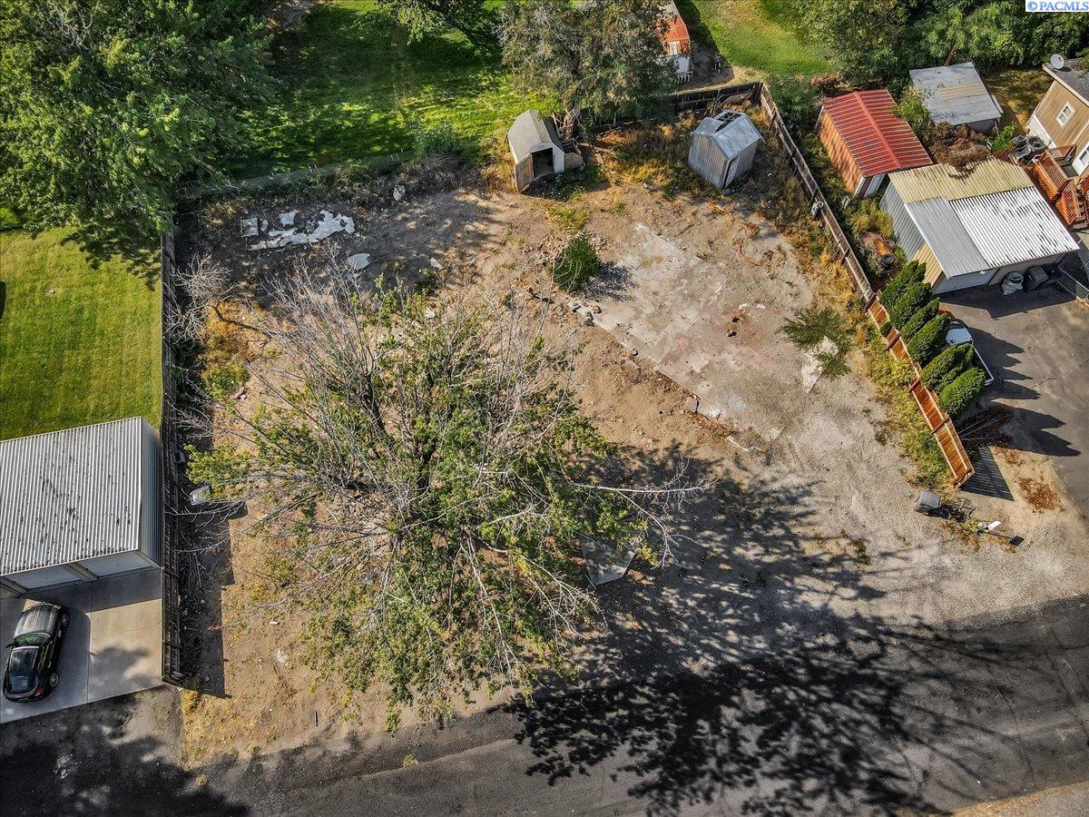 Aerial view of a cleared vacant lot bordered by fencing, trees, and neighboring sheds.