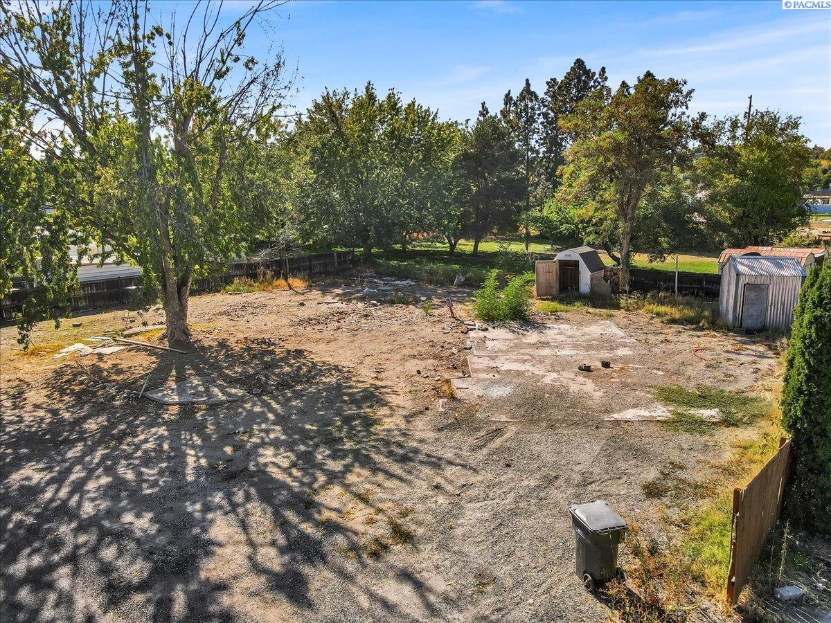 Cleared vacant lot with mature trees, fencing, and two storage sheds.