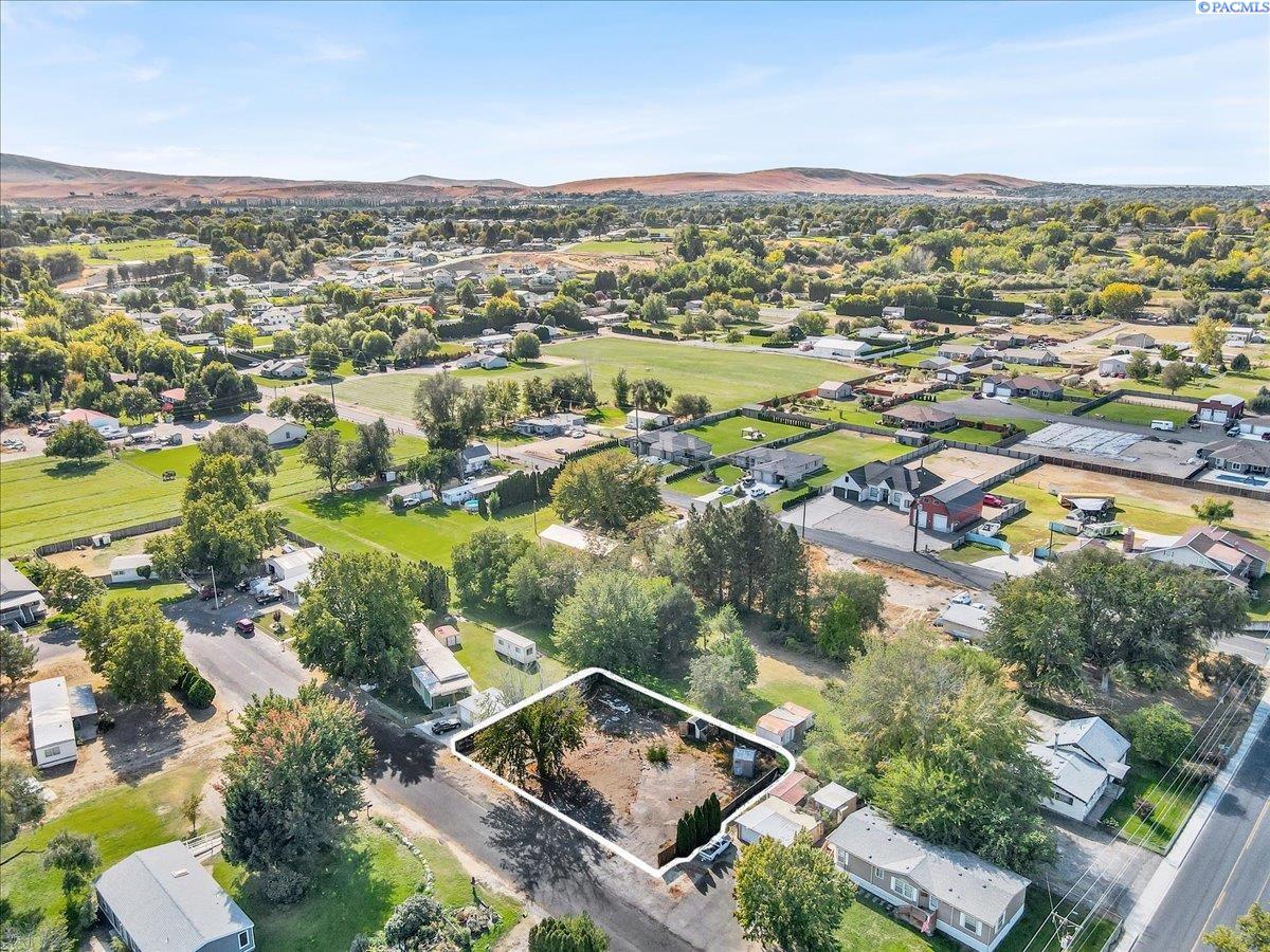 Outlined vacant lot among homes and trees, with rolling hills in the distance.