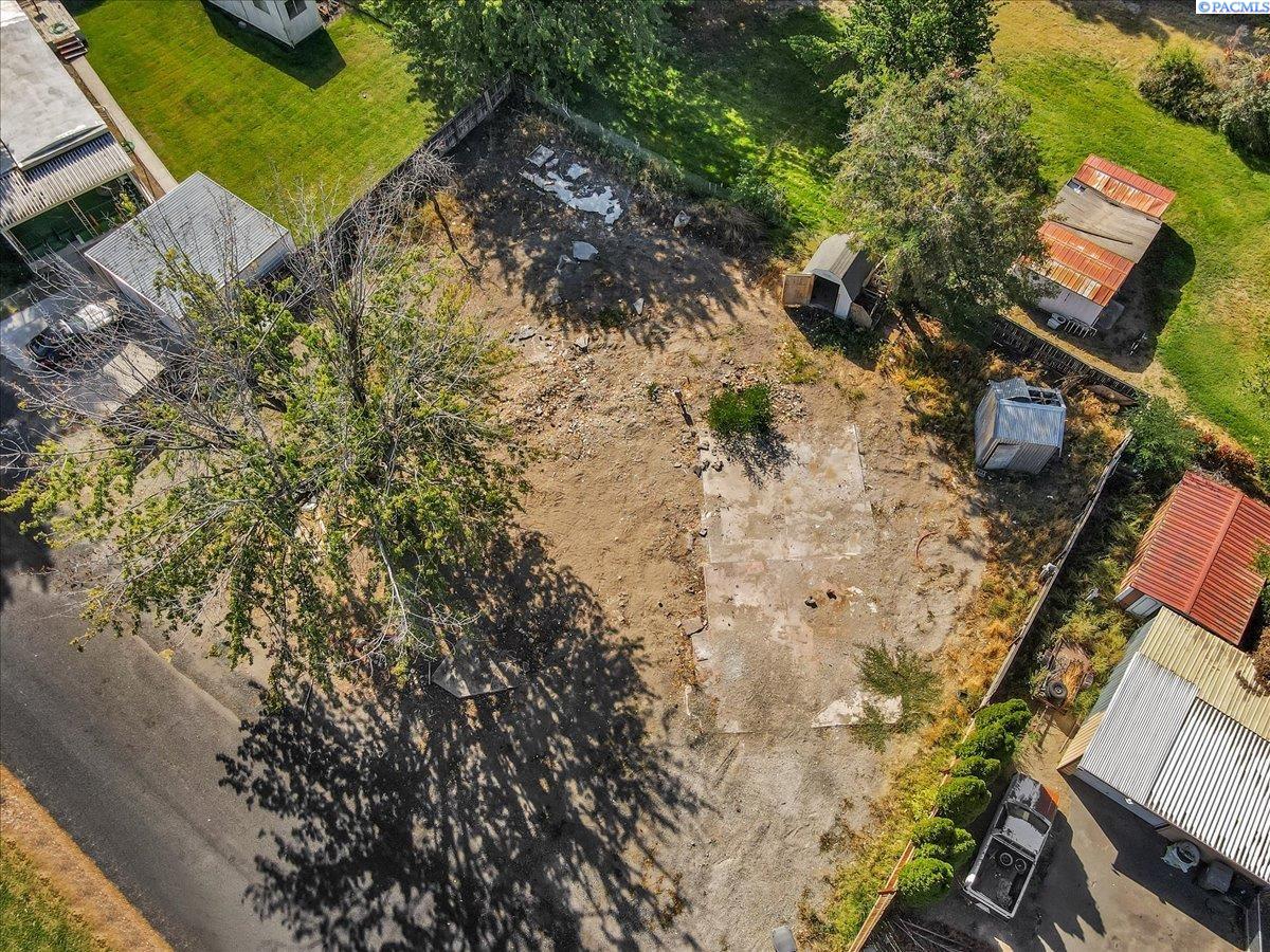 Aerial view of a cleared lot with concrete slabs, mature trees, and neighboring sheds.