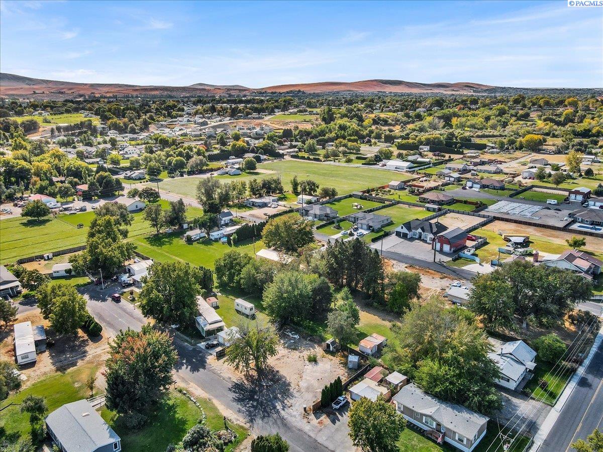 Aerial view of a vacant lot among homes, mature trees, and open fields.