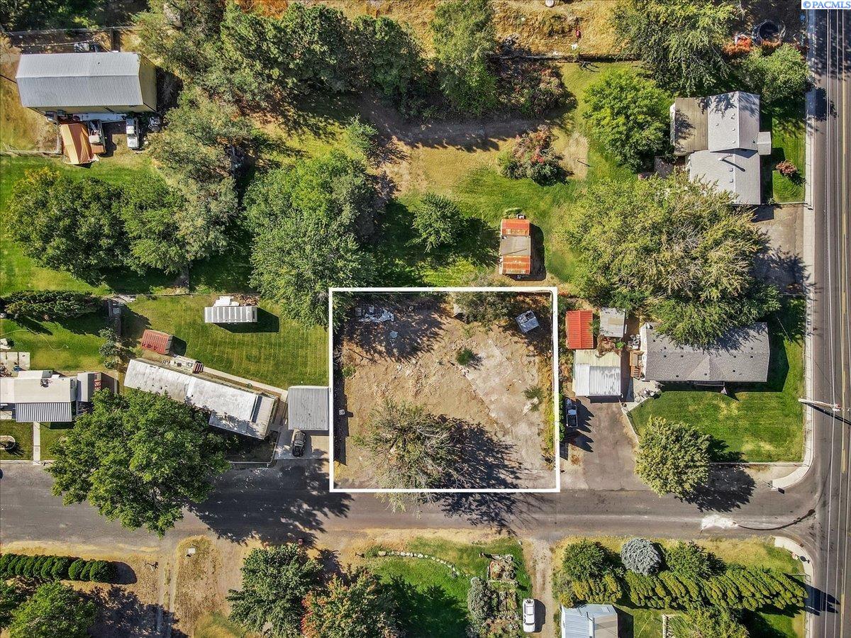Aerial view of a cleared lot outlined in white among neighboring homes and trees.