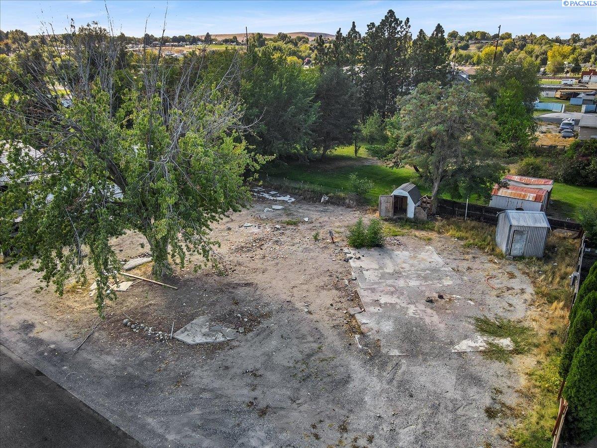 Aerial view of a cleared lot with concrete pads, mature trees, and sheds.