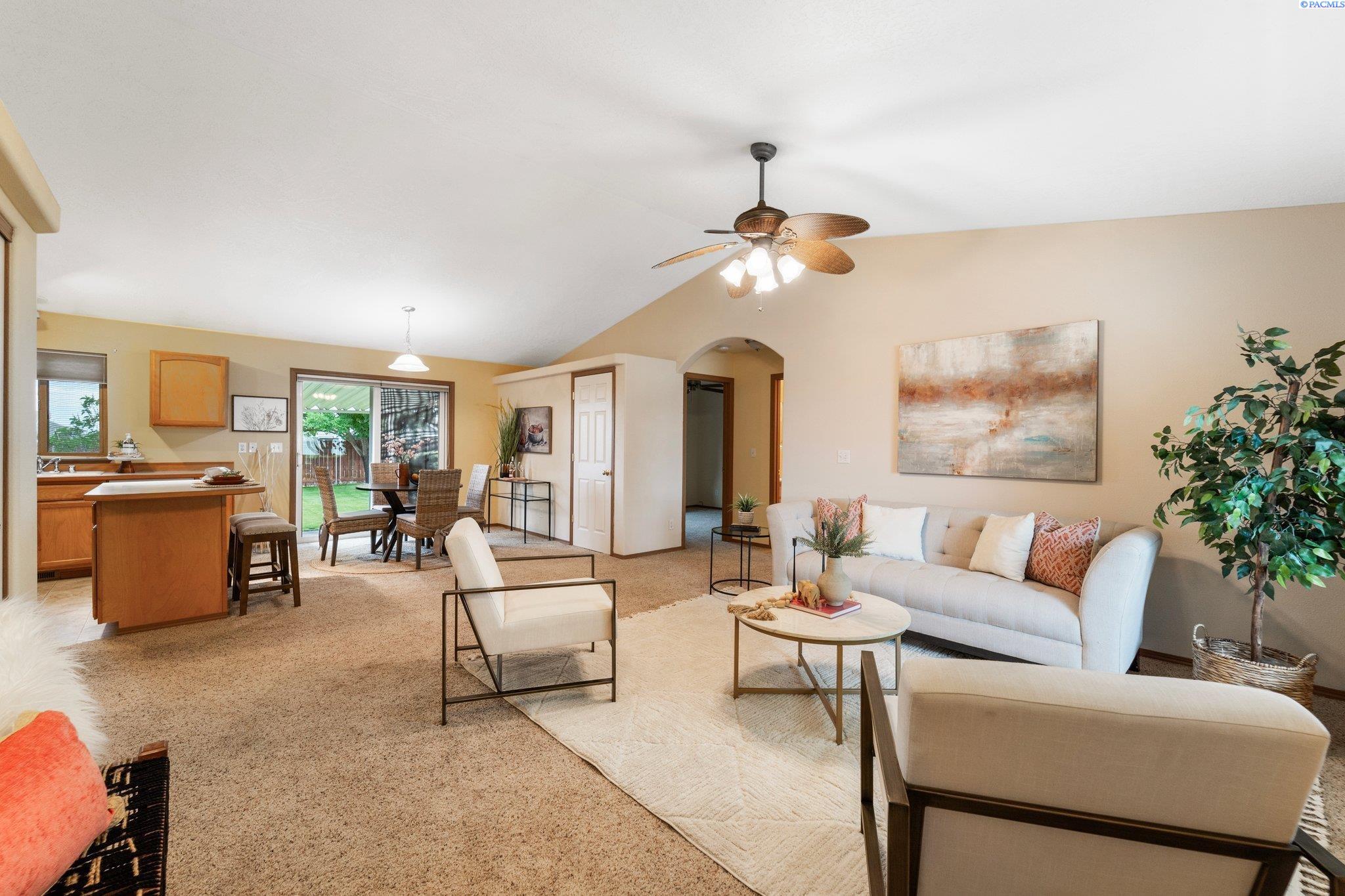 Open-plan living room with white seating, a ceiling fan, and dining area beside sliding glass doors.