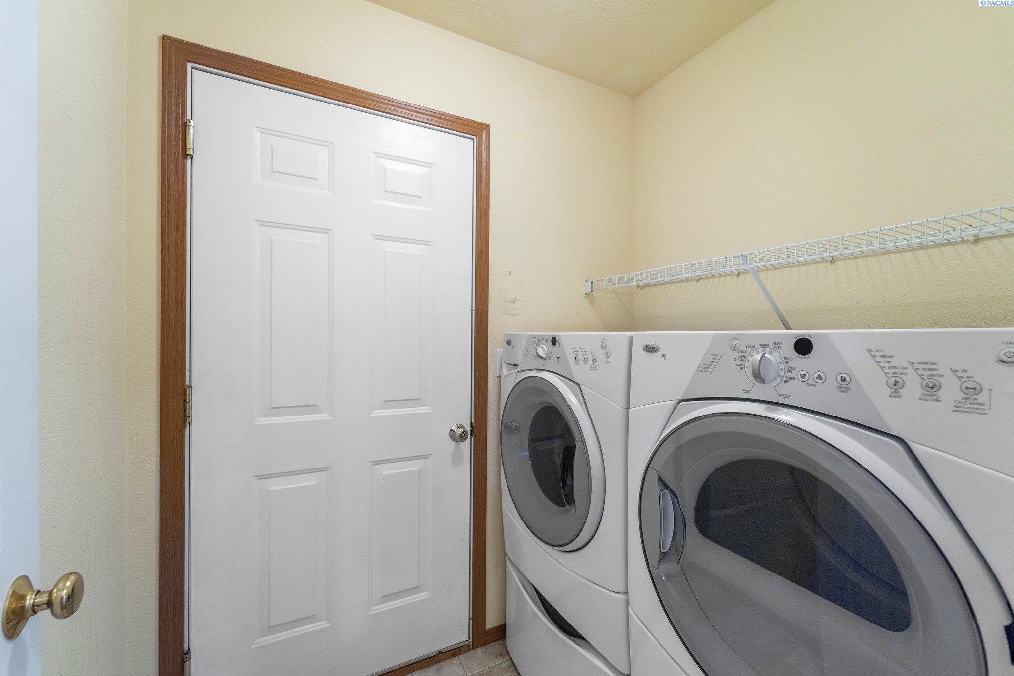 Laundry room with front-loading washer and dryer beneath a long wire shelf.