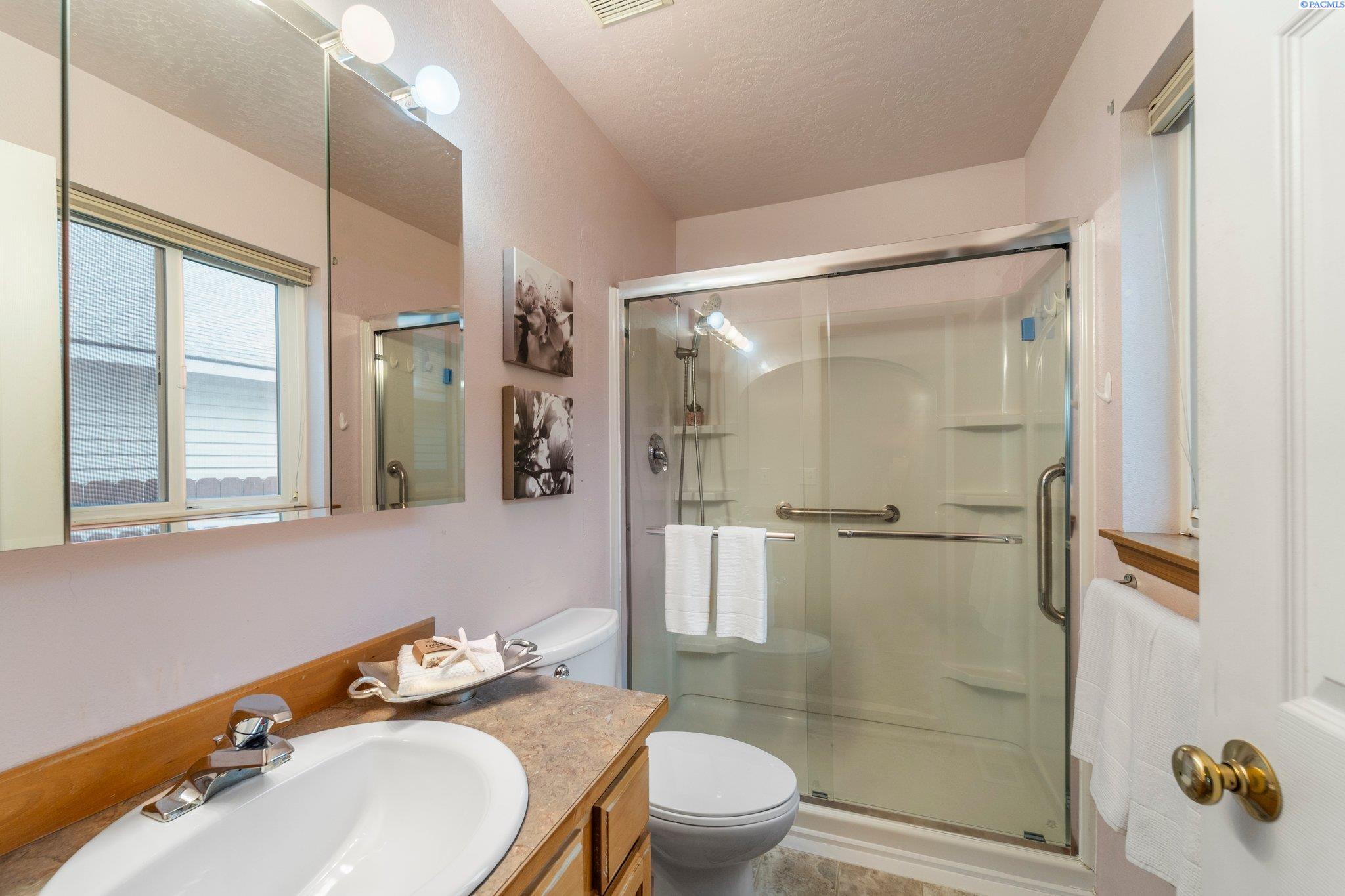 Bathroom with a wood vanity and glass-enclosed shower featuring grab bars and built-in shelves.
