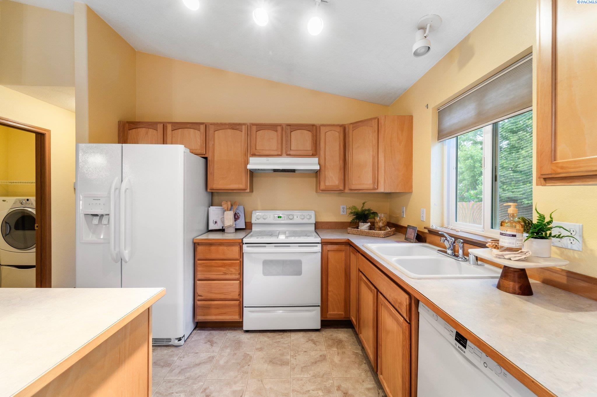 Kitchen with wood cabinets, white appliances, and a double sink beneath a window.