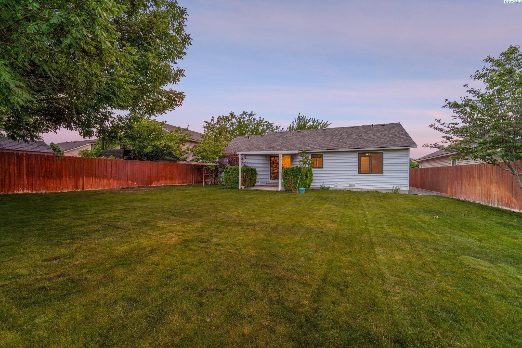 Home’s rear exterior with a covered patio, spacious lawn, and wooden privacy fence.