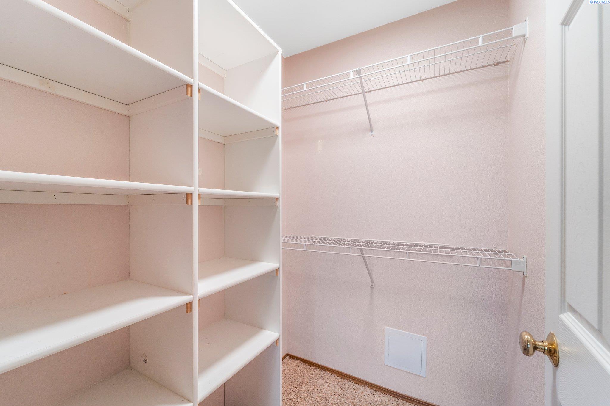 Walk-in closet with built-in shelving and two wire clothing racks.