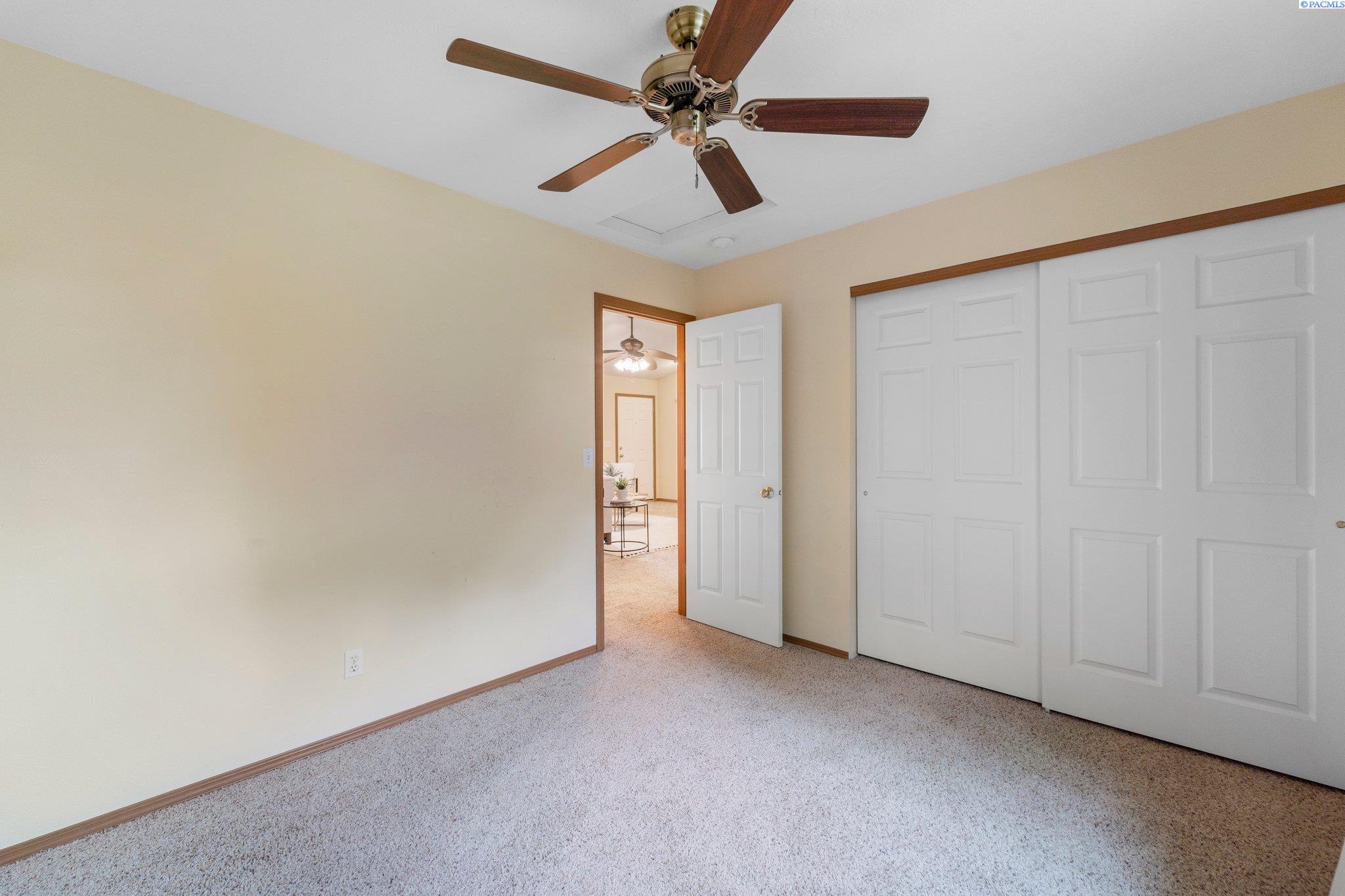 Empty carpeted bedroom with a ceiling fan, sliding closet doors, and an open doorway.