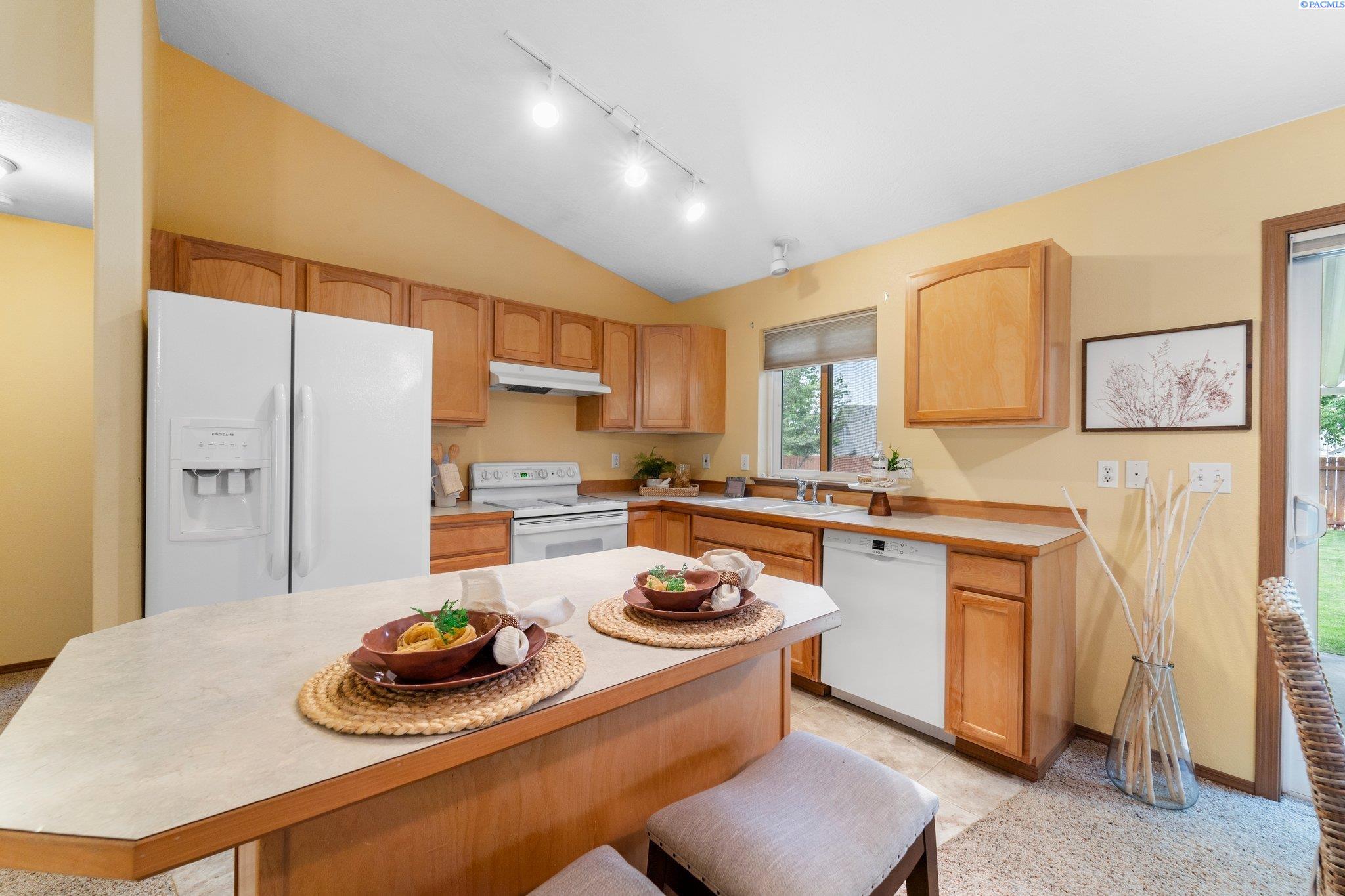 Staged kitchen with wood cabinets, a large peninsula, and white appliances.
