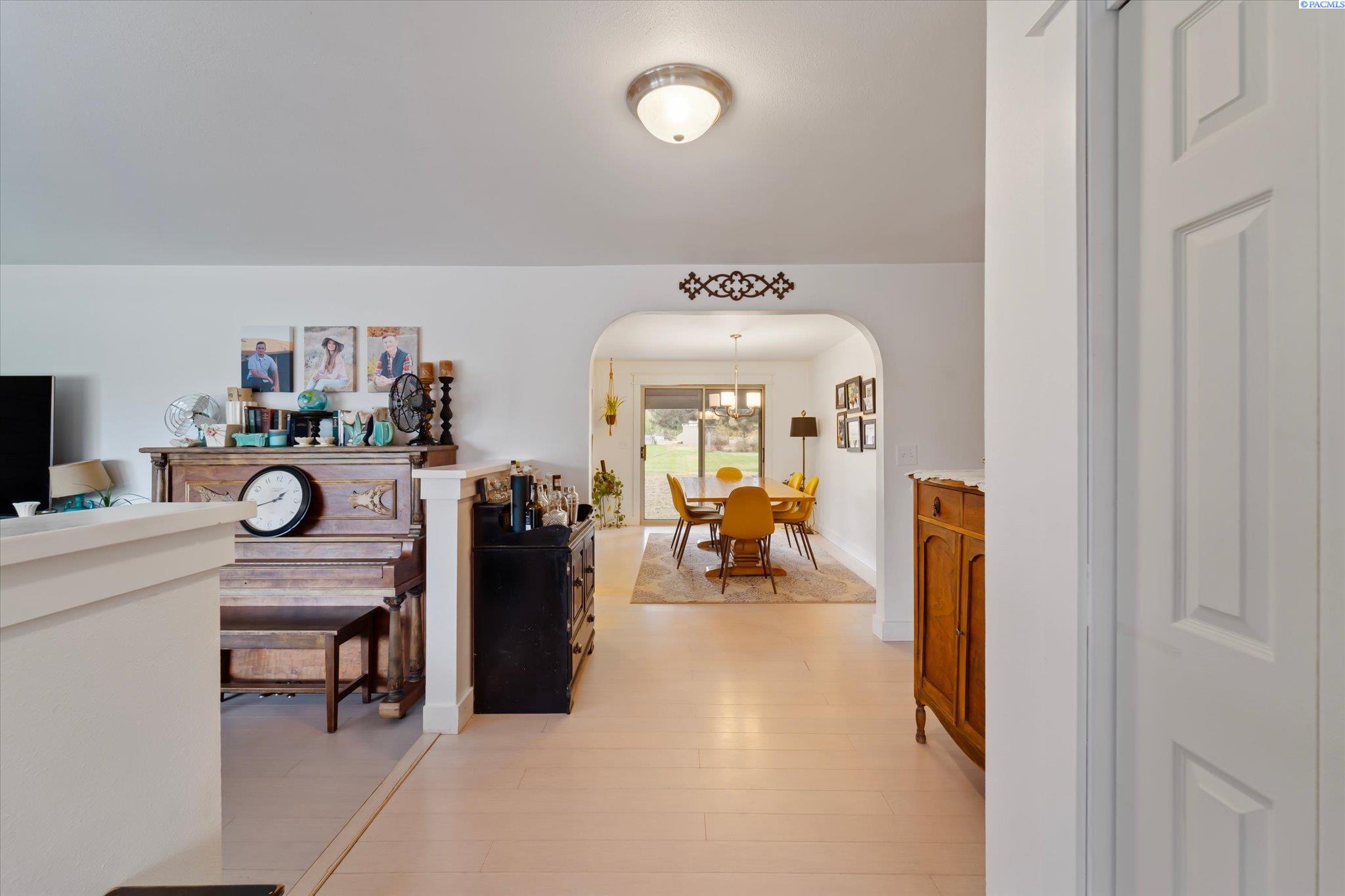 Entry hall opens through an arch to a dining area with mustard-yellow chairs and a sliding glass door.