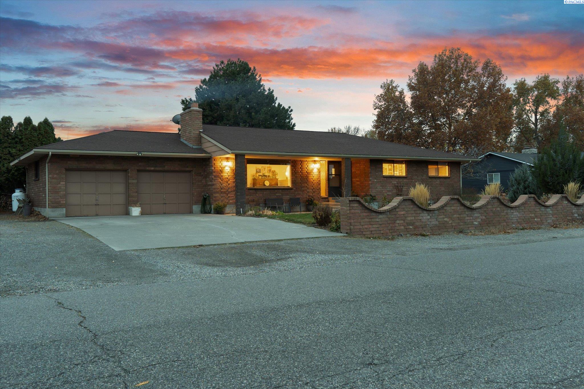Single-story brick house with two garage doors and a curved brick wall at dusk.