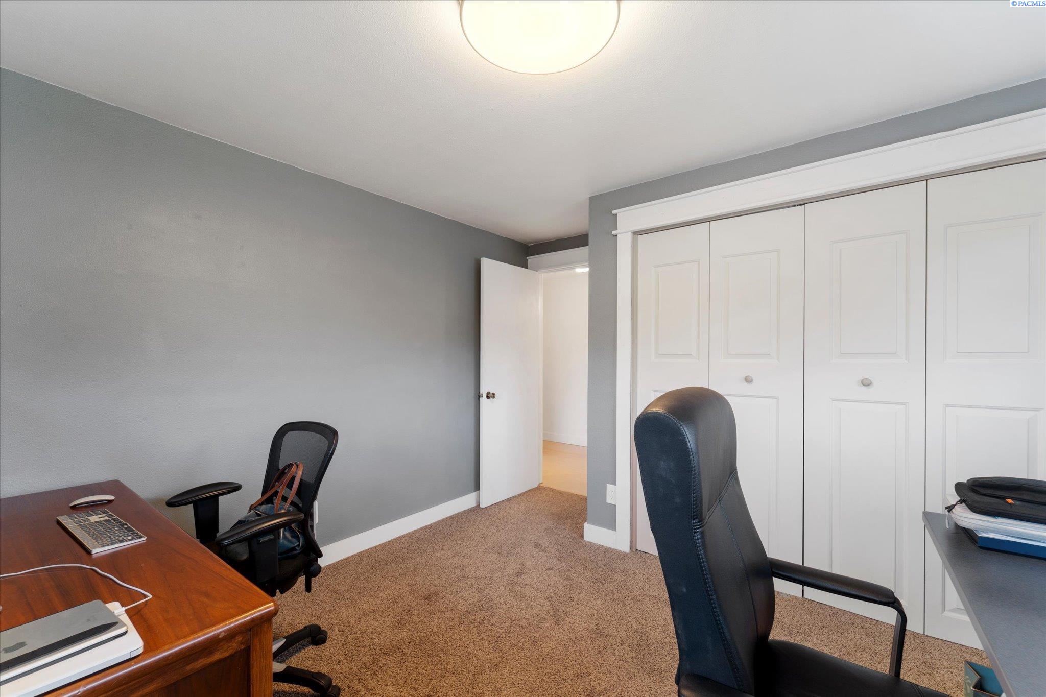 Furnished home office with a wooden desk, office chairs, and white closet doors.