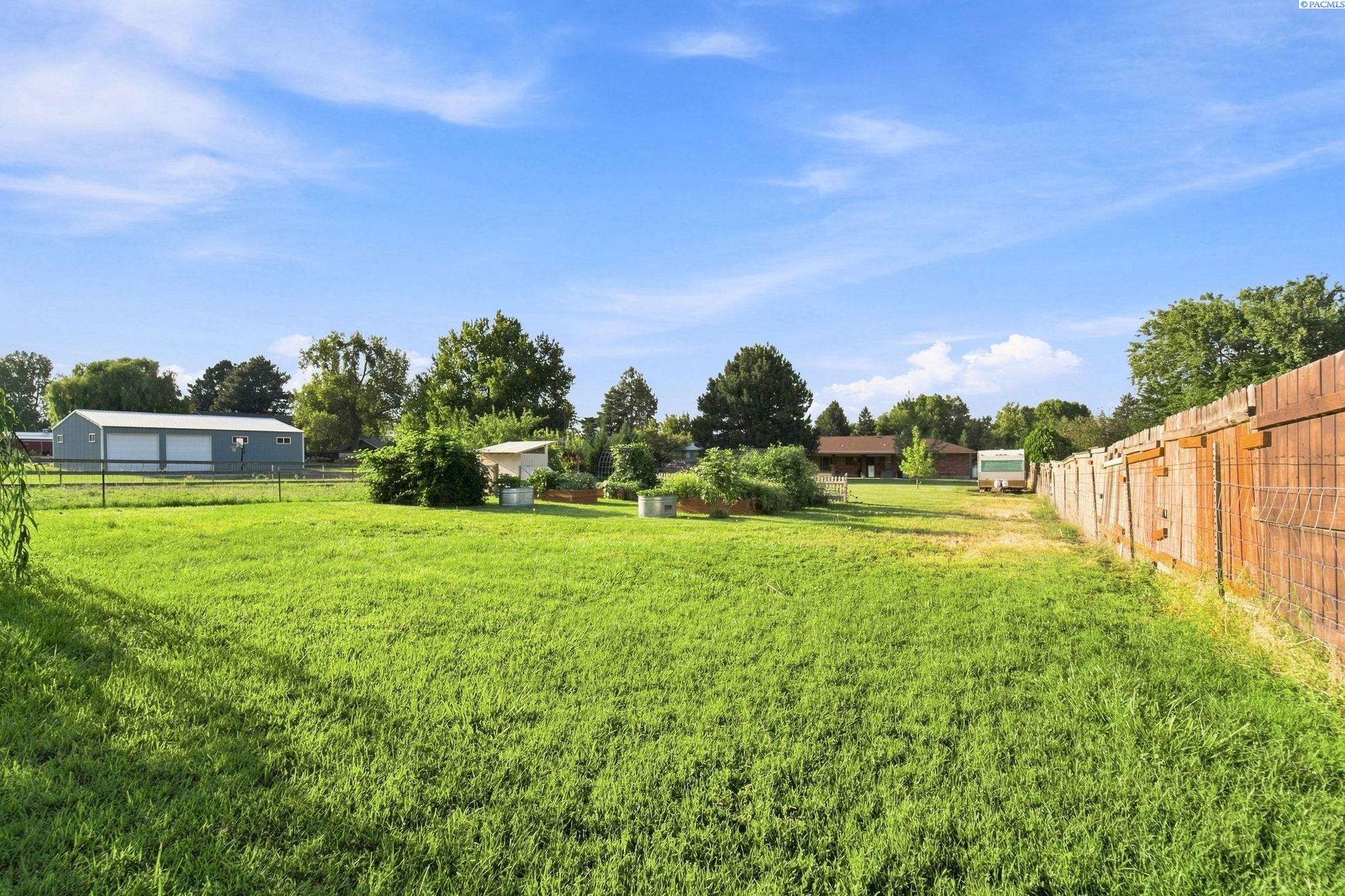 Large grassy yard with raised garden beds, mature trees, and a long wooden fence.