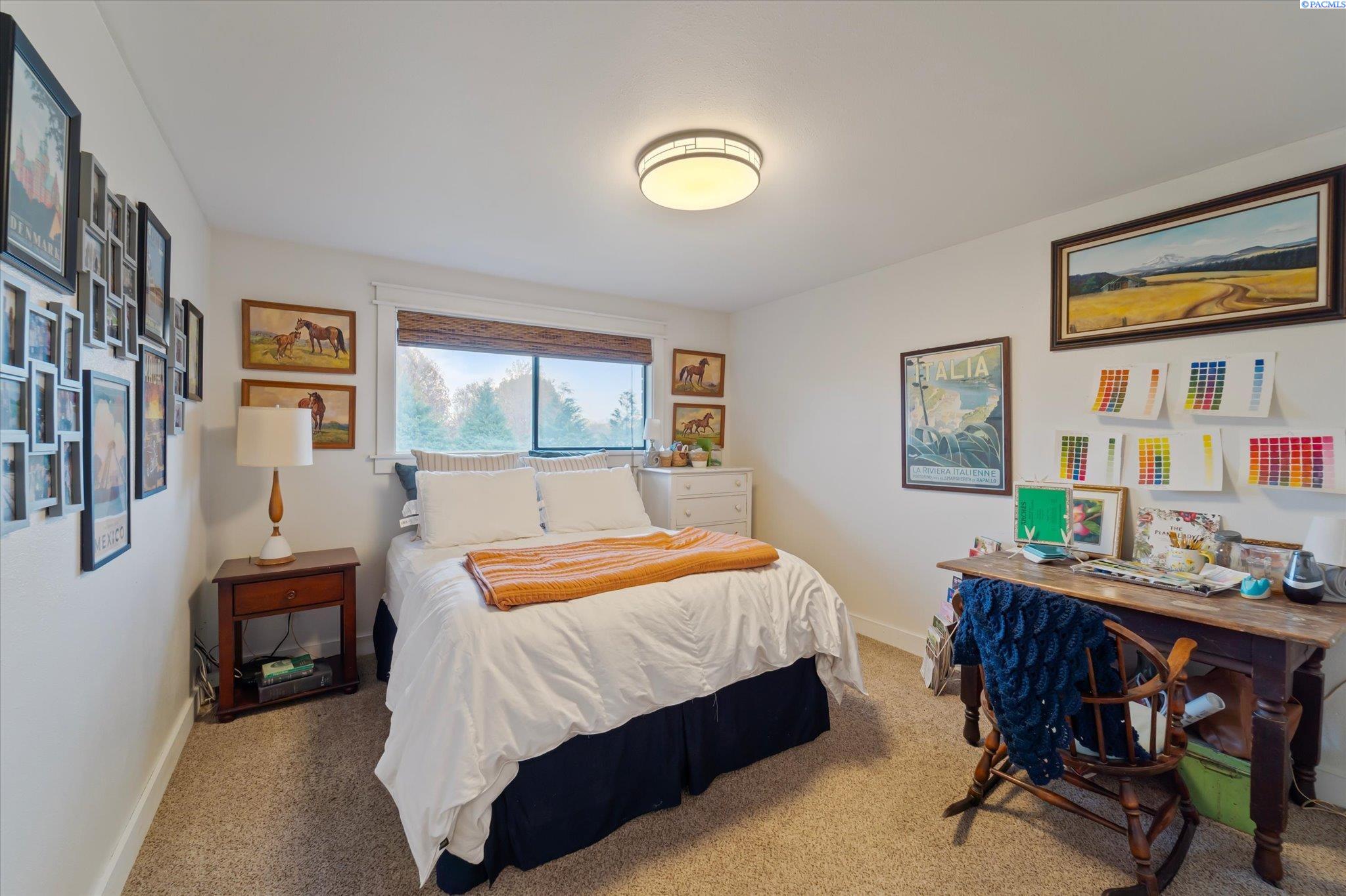 Bedroom with a white bed, orange throw, wall art, and a wooden desk with color swatches.