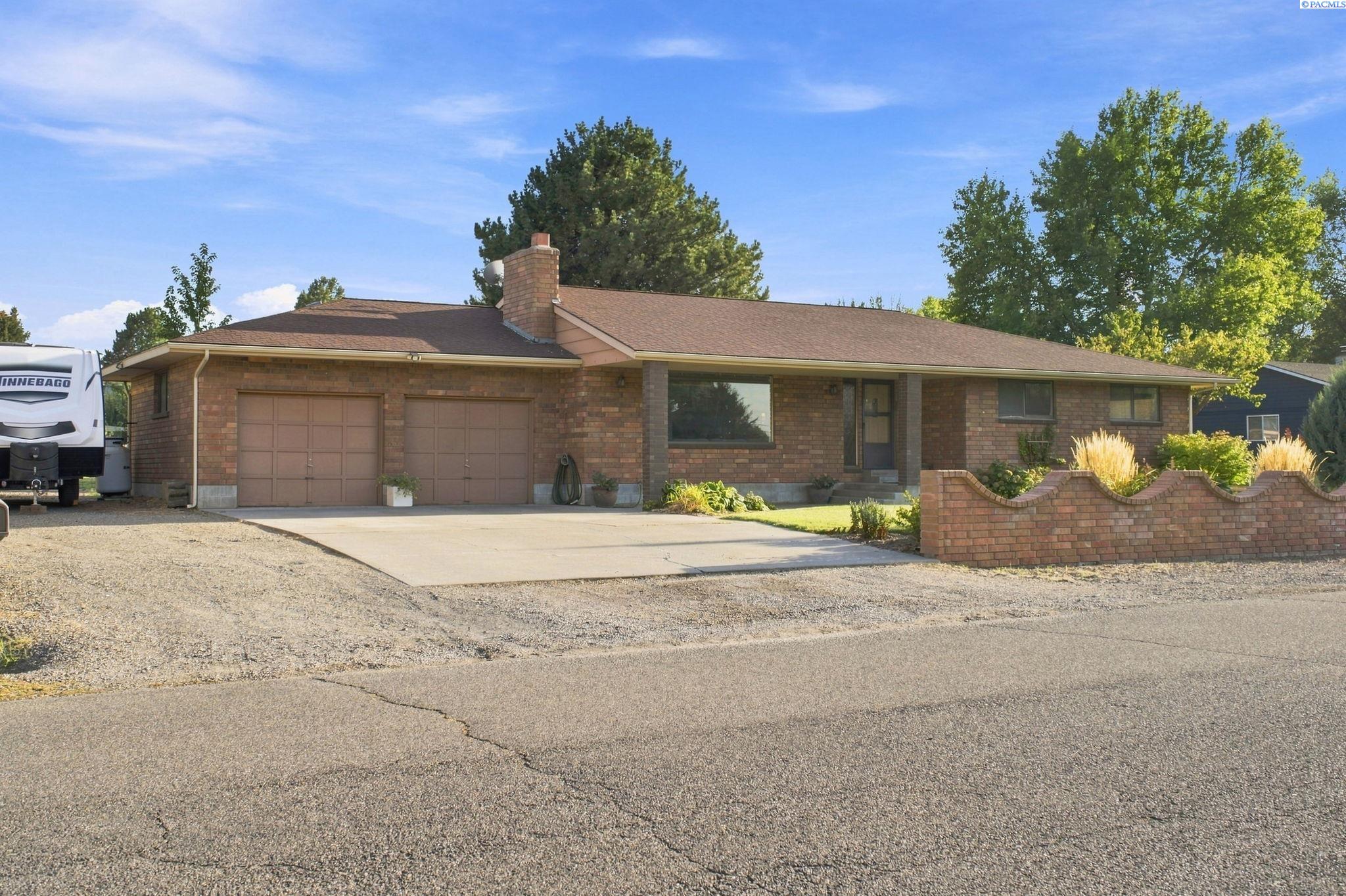 Single-story brick ranch house with two garage doors and a curved brick garden wall.