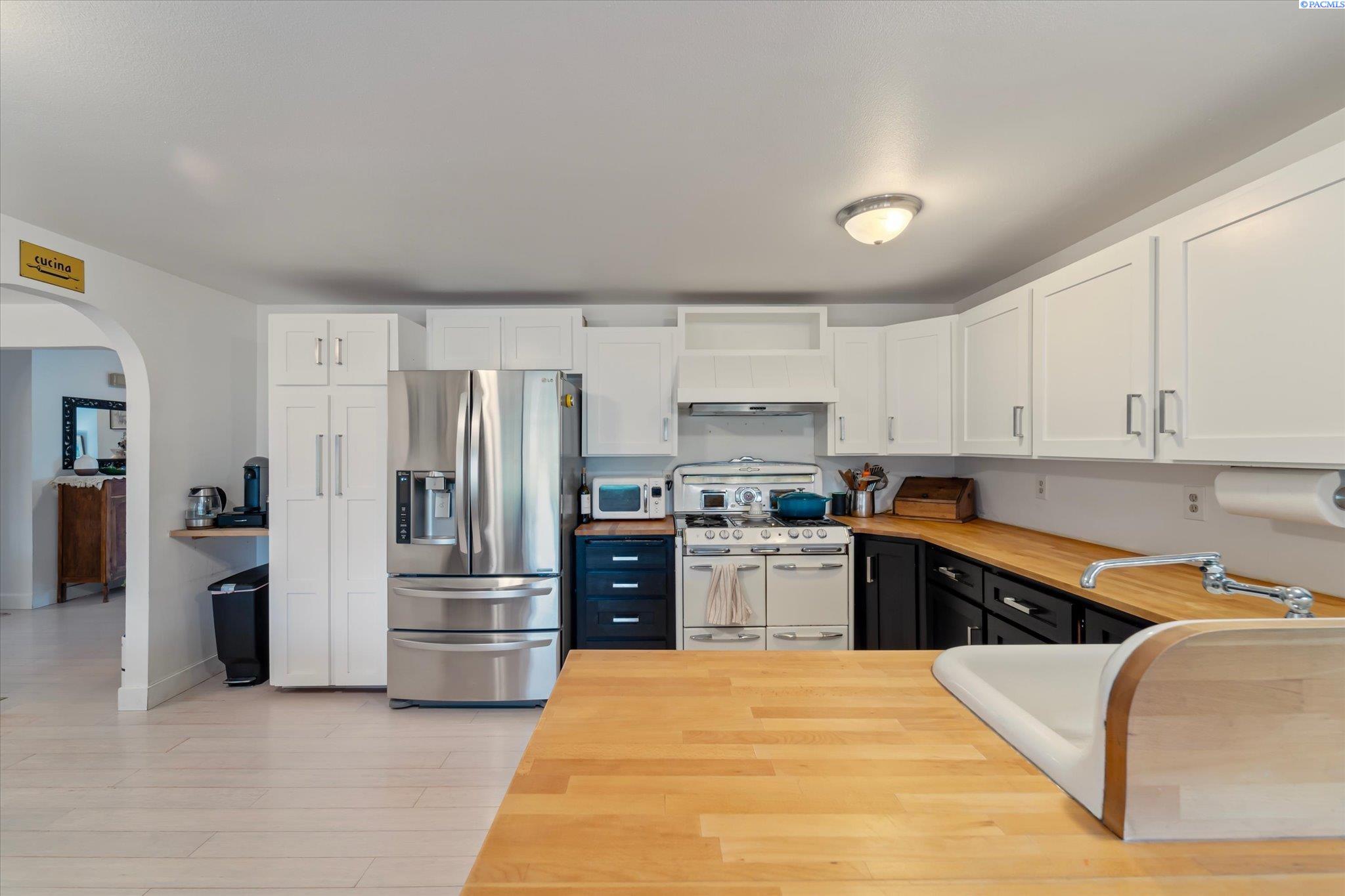 Kitchen with white cabinets, stainless steel refrigerator, vintage-style range, and broad butcher-block counter.