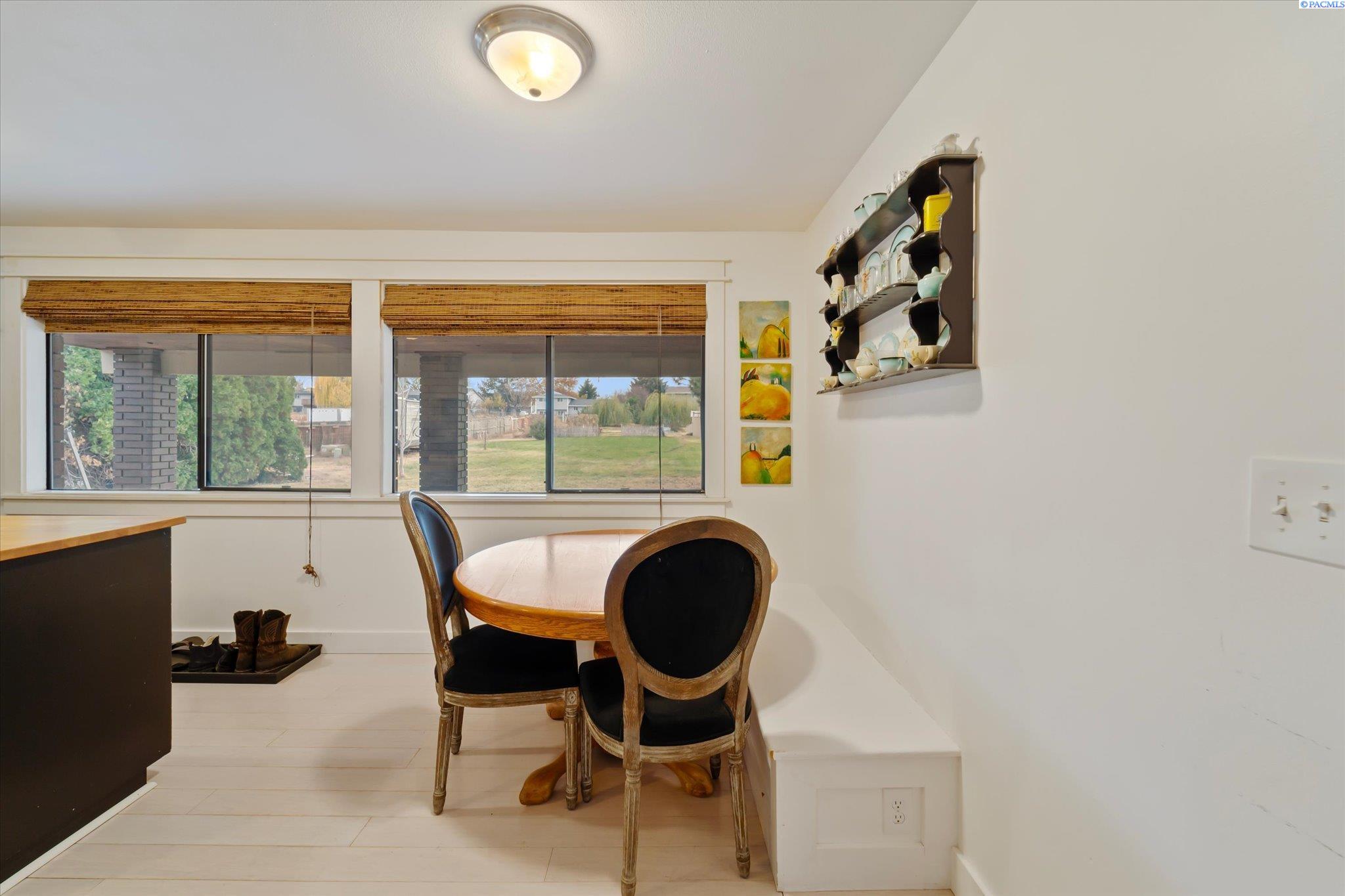 Dining nook with a round wooden table, dark chairs, and wide windows overlooking the backyard.