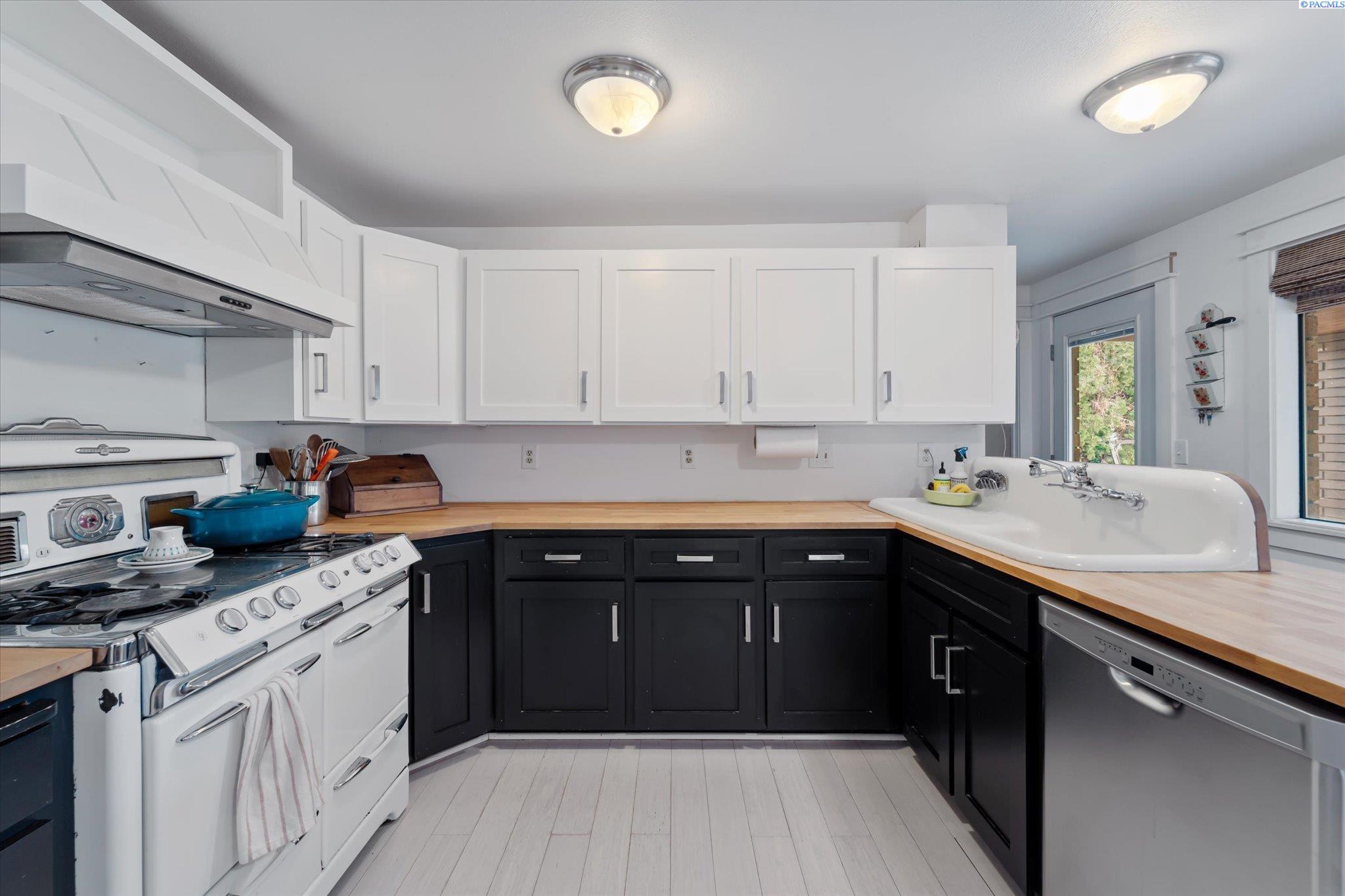 Kitchen with black and white cabinets, butcher-block counters, a farmhouse sink, and a vintage-style range.