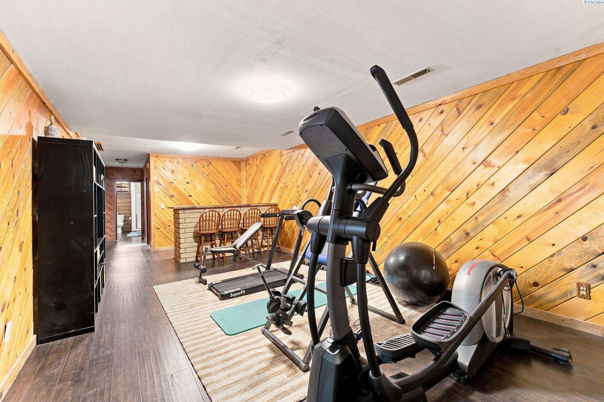 Home gym with exercise equipment and diagonal honey-colored wood-paneled walls.